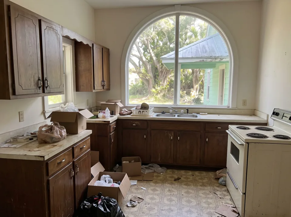 Illustration: a dated kitchen with old wood cabinets, laminate counters and a white stove at a mint green historic Delray Beach home with arched windows, standing-seam metal roof and big shade trees, clear midday sun