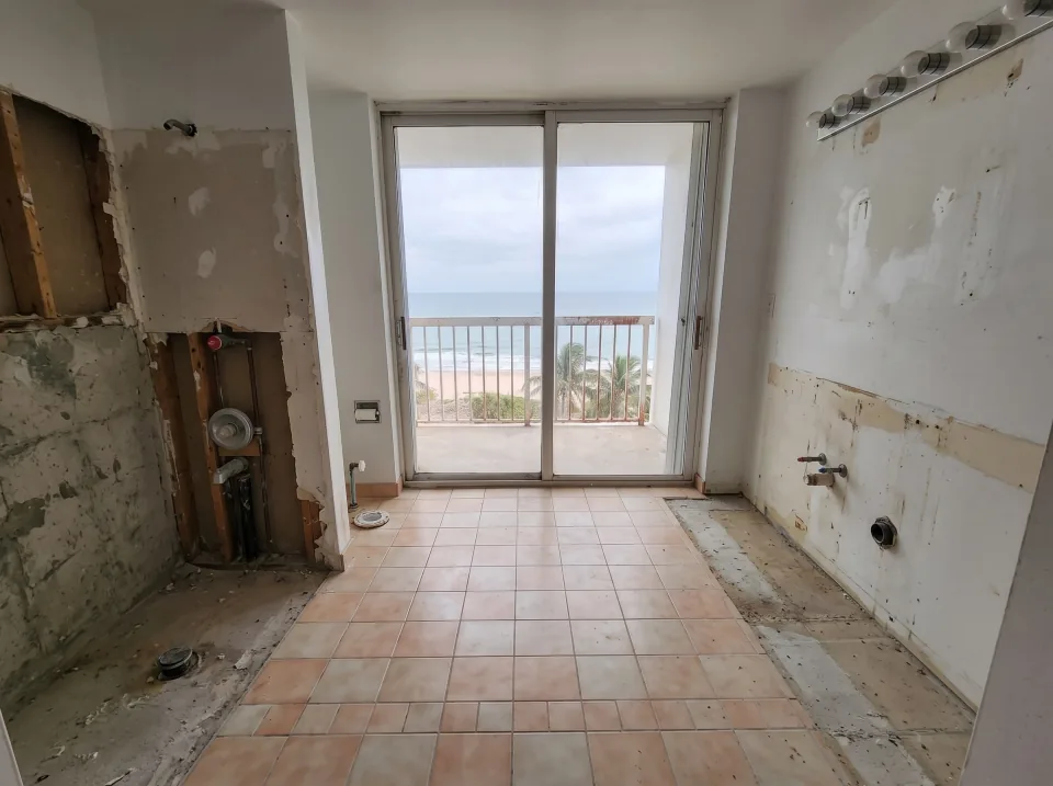 Illustration, after: the tile, tub, toilet and vanity removed, with bare walls, capped plumbing, a swept floor and the window visible