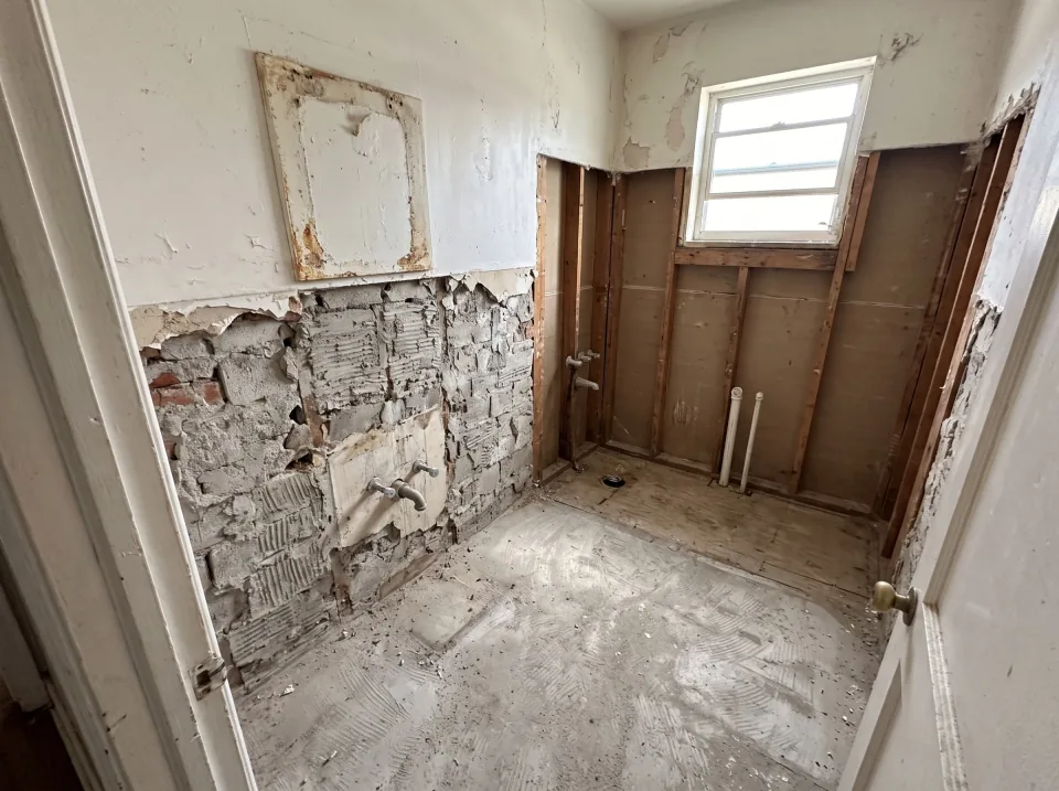 Illustration, after: the tile, tub and sink removed, with bare walls, capped plumbing and a swept floor