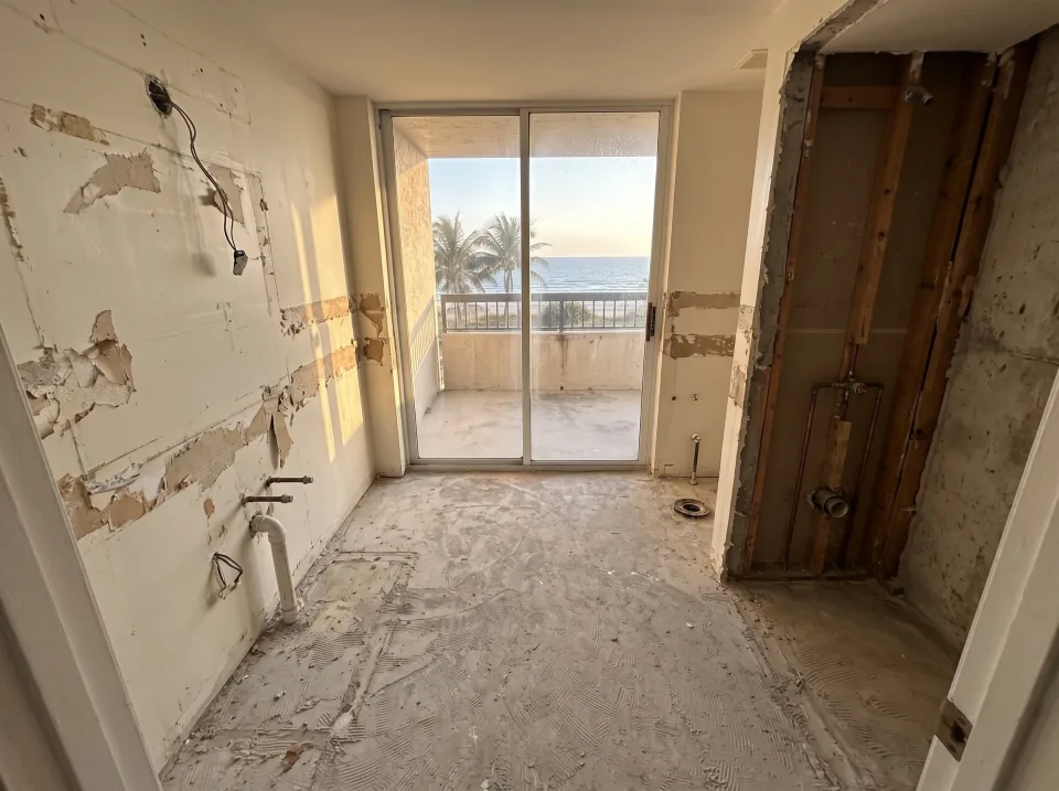 Illustration, after: the tile, tub, toilet and vanity removed, with bare walls, capped plumbing, a swept floor and the window visible