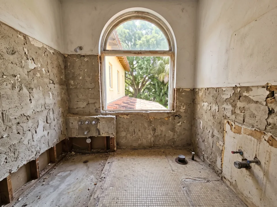 Illustration, after: the tile, tub, toilet and vanity removed, with bare walls, capped plumbing, a swept floor and the window visible