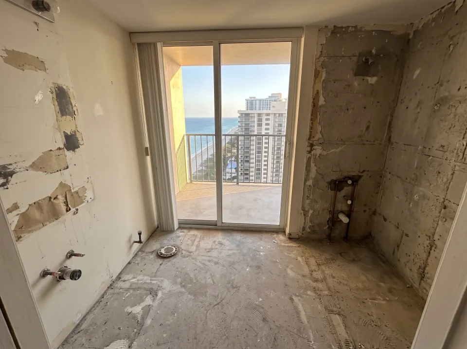 Illustration, after: the tile, tub, toilet and vanity removed, with bare walls, capped plumbing, a swept floor and the window visible
