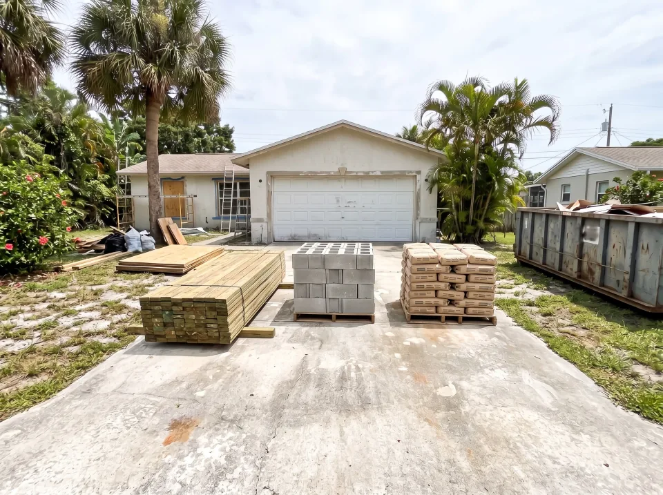 Illustration, after: new materials neatly stacked on the driveway: pressure-treated lumber, a pallet of concrete block and bags of mortar